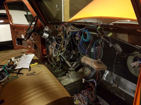 1978 Ford Bronco - The interior of a vehicle shows a complex mess of exposed wiring and an orange hood is open.