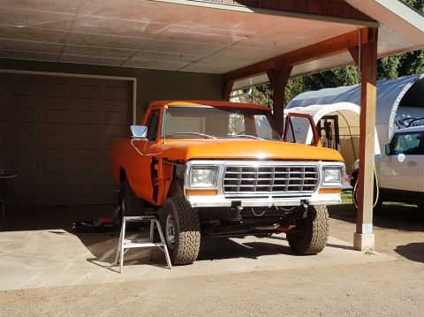 1978 Ford Bronco - Orange pickup truck undergoing repairs, with its front end disassembled and the vehicle elevated.