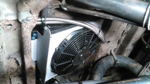 1978 Ford Bronco - Black electric cooling fan bolted to an aluminum shroud with a braided line, installed in a rusty engine compartment.