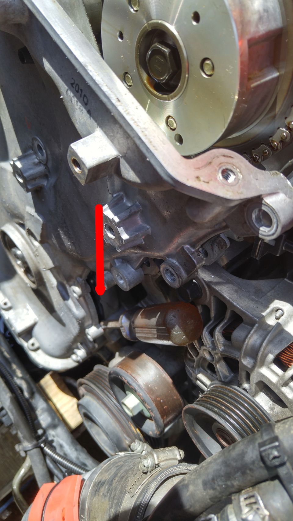 Close-up of engine timing chain components with a red arrow pointing to a sensor. The year 2010 is visible on a bracket