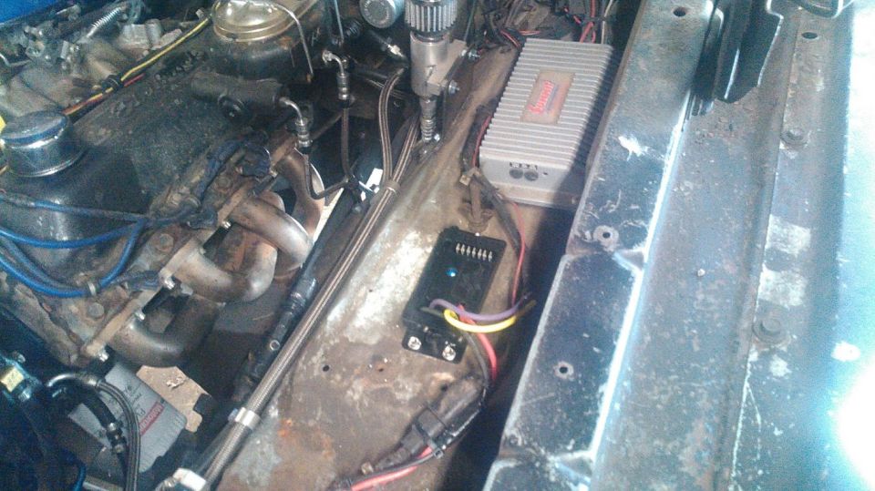 Engine bay with a V8 engine, headers, and aftermarket amplifier and control box