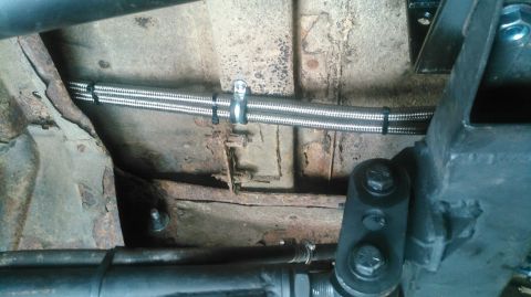1978 Ford Bronco - Braided hoses are routed along the rusty undercarriage of a vehicle.