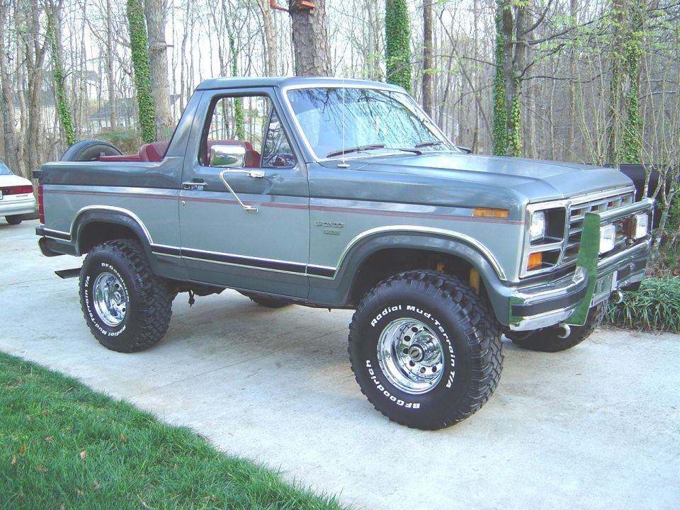 Two-tone gray topless Ford Bronco, lifted with mud tires and chrome brush guard, on driveway.