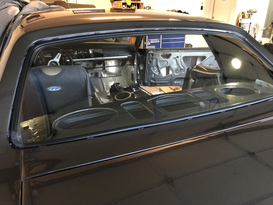 Car interior with doors removed, showing bare metal and roll cage. T-shirt on driver's seat
