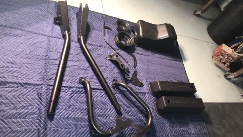 1979 Ford Bronco - Various black metal automotive parts are arranged on a blue quilted mat, with a Supermotors.net logo visible.