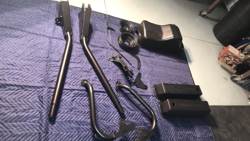 Black metal automotive parts laid out on a blue quilted mat, including valve covers and suspension components