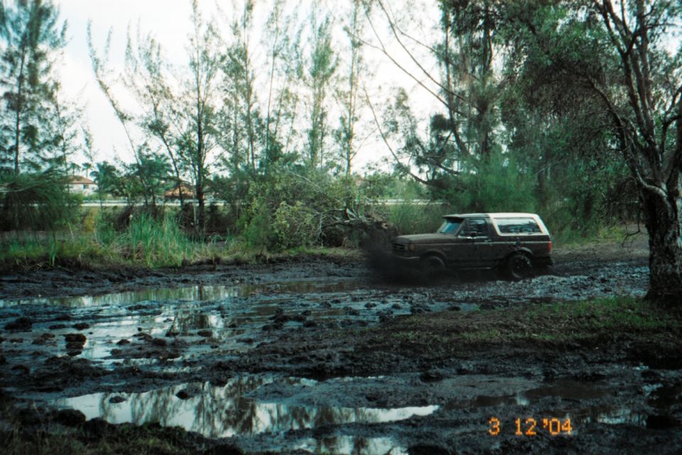 Mud-covered two-tone SUV driving through a muddy field, splashing mud