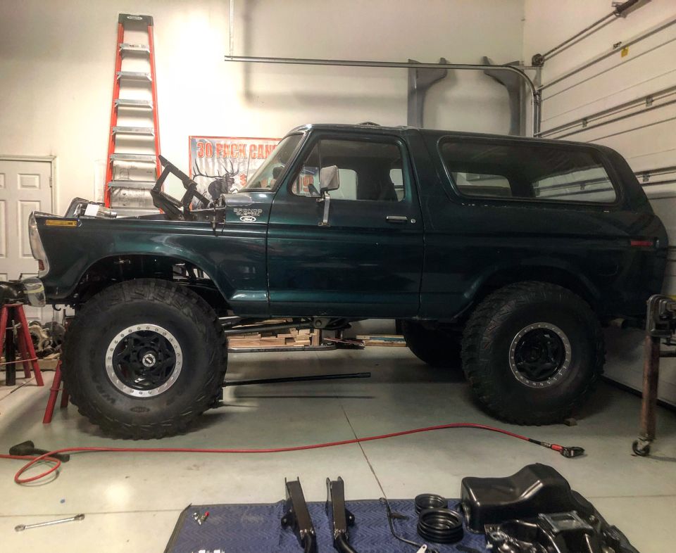 Dark green 1978 Ford Bronco, lifted, in garage with hood open and parts on floor