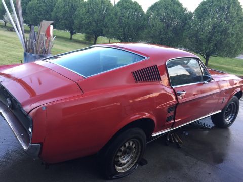 1967 Ford Mustang - This red 1967 Ford Mustang coupe is parked outdoors on a wet surface.