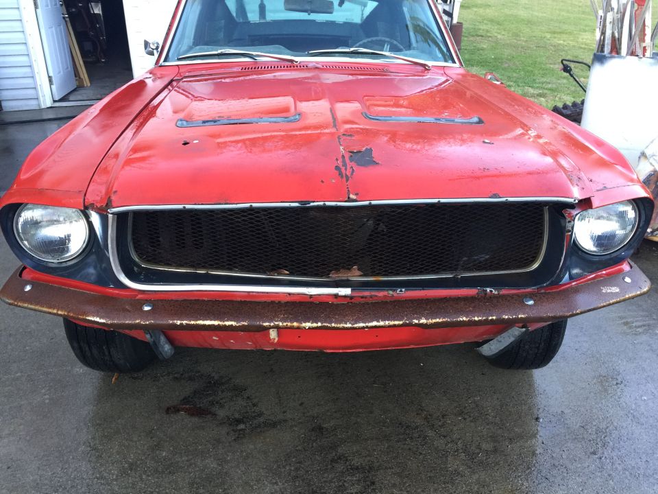 Front view of a red 1967 Ford Mustang with a rusty bumper and grille