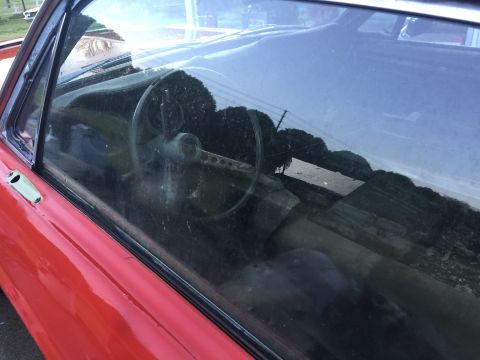 1967 Ford Mustang - The interior of a red 1967 Ford Mustang is visible through a dirty side window.
