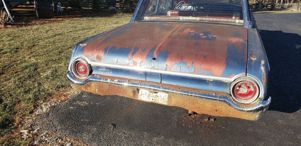 Rear view of a rusty 1962 Ford Galaxie with peeling paint and chrome bumper