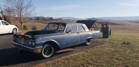 1962 Ford Galaxie - A blue sedan sits parked outdoors with its hood and trunk open, next to a white SUV.