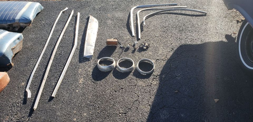 Car trim pieces, seat cushions, and three headlight bezels laid out on asphalt