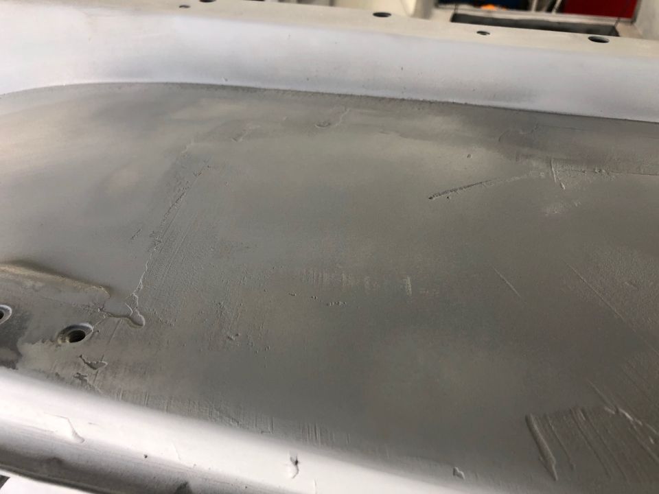 Primed car body panel with visible sanding marks and some small holes
