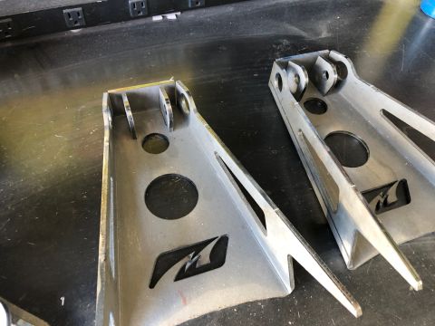 1992 Jeep Wrangler - Pair of metal suspension brackets shown on a workbench surface.