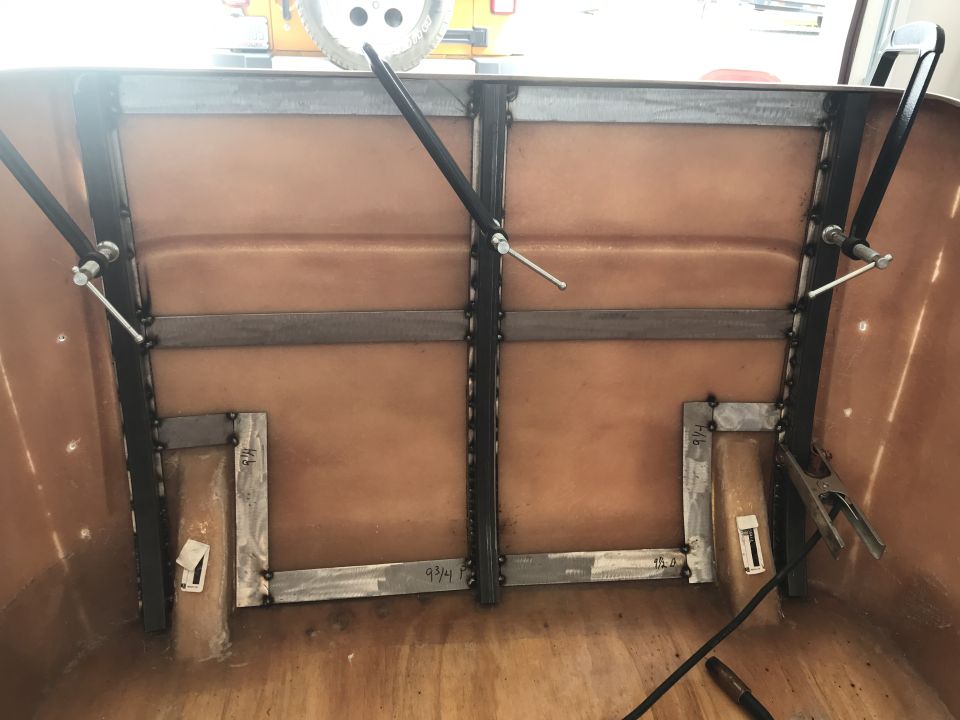 Vehicle bed interior with custom metal bracing and brown fiberglass lining. Visible measurements on metal brackets
