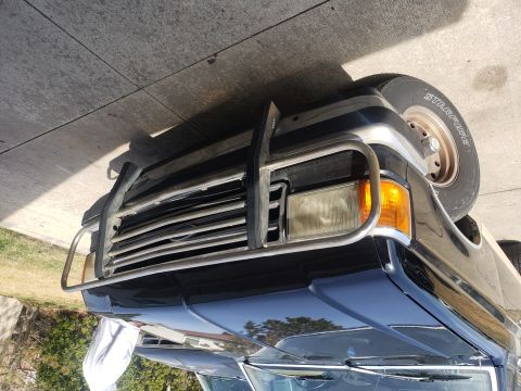 1995 Ford Bronco - The front grille and bumper of a dark blue truck are visible, equipped with a large brush guard.