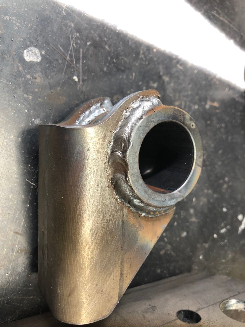 Welded metal bracket with a circular opening, showing rough weld marks and brushed metal texture