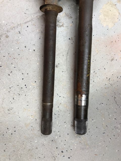 1992 Jeep Wrangler - Two axle shafts, likely for a Jeep Wrangler, are shown side-by-side on a concrete surface. One shaft has visible yellow markings.