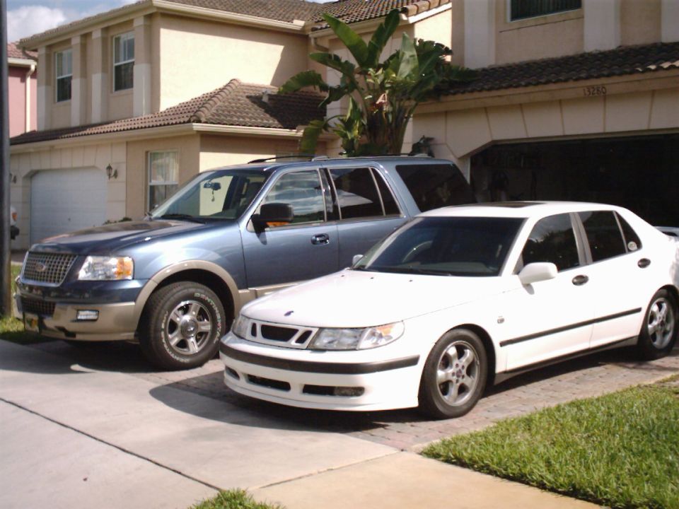 White Saab 9-5 sedan parked beside a blue Ford Expedition SUV in a driveway