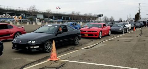 2006 Mitsubishi Evolution - A line of cars, including a black coupe and a red Camaro, are staged at a racetrack.