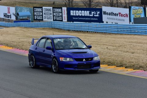 2006 Mitsubishi Evolution - A blue Mitsubishi Lancer Evolution VIII navigates a race track, displaying its aggressive styling and performance modifications.