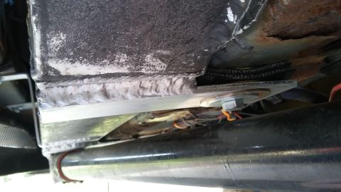 Welded metal bracket attached to vehicle frame with bolts and wiring visible