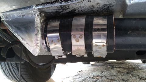 Exhaust pipe secured with three metal hose clamps, showing welds on a metal bracket