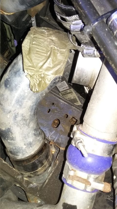 Engine bay showing a large metal pipe, a blue silicone coupler, and a yellow plastic bag covering some compone