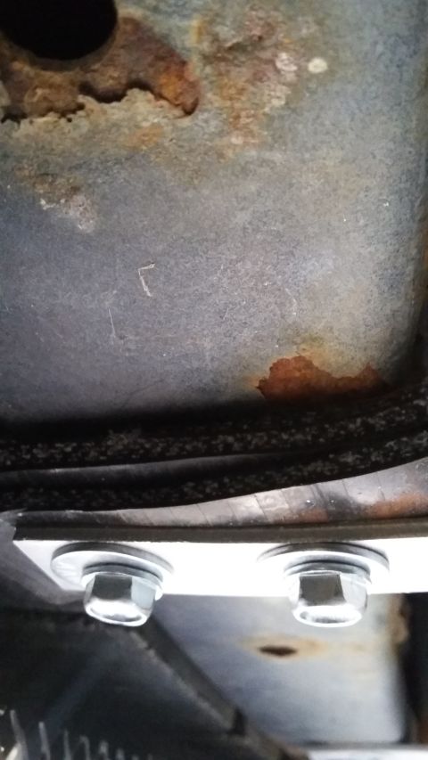 Underbody of a vehicle showing rust patches and two bolts securing a metal plate