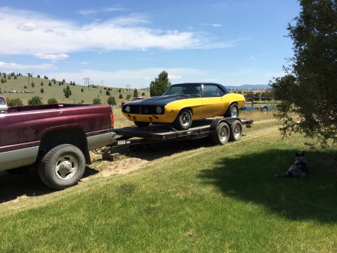 1969 Chevrolet Camaro - A yellow and black 1969 Chevrolet Camaro is transported on a trailer, with a maroon truck in the foreground.