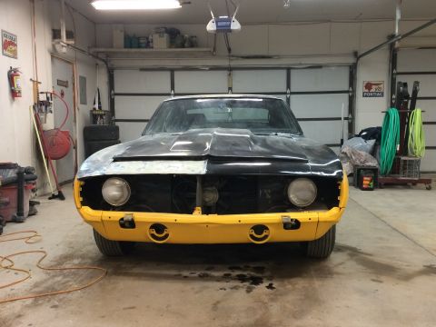 1969 Chevrolet Camaro - Frontal view of a 1969 Chevrolet Camaro in a garage, showing its yellow bumper and partially prepped black hood during restoration.