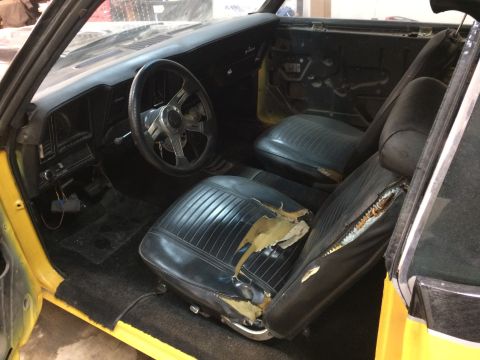 1969 Chevrolet Camaro - Interior view of a yellow 1969 Chevrolet Camaro showing damaged black vinyl seats and dashboard.