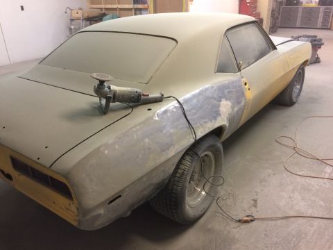 1969 Chevrolet Camaro - A 1969 Chevrolet Camaro is in a workshop, covered in primer and dust, with an angle grinder resting on its trunk.