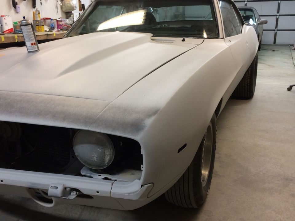 1969 Chevrolet Camaro body in primer, front quarter view, showing primer hood and fender, with a spray can on the hood
