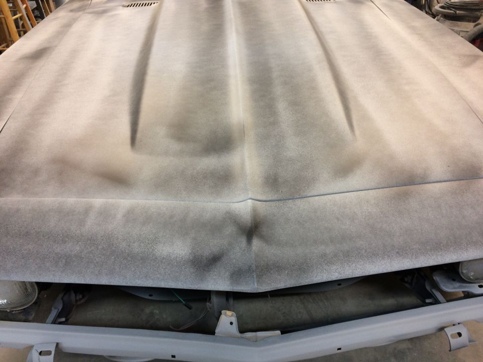 Camaro hood in gray primer with guide coat sanding, viewed from the front in a body shop