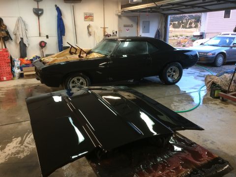 1969 Chevrolet Camaro - A black 1969 Chevrolet Camaro is parked in a garage with its hood removed, revealing a partially covered engine bay.