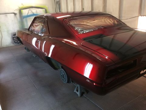 1969 Chevrolet Camaro - A red 1969 Chevrolet Camaro is being worked on in a paint booth, with its windows covered in tape.