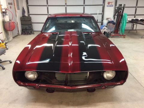 1969 Chevrolet Camaro - Front view of a red 1969 Chevrolet Camaro with black racing stripes, parked in a garage.