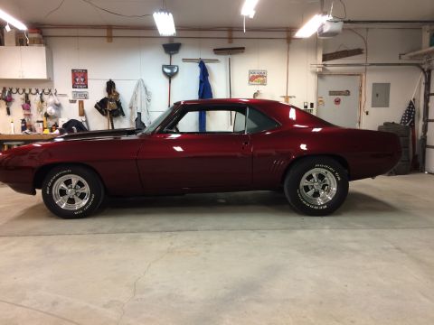 1969 Chevrolet Camaro - A deep red 1969 Chevrolet Camaro coupe is parked inside a garage, its classic body style.