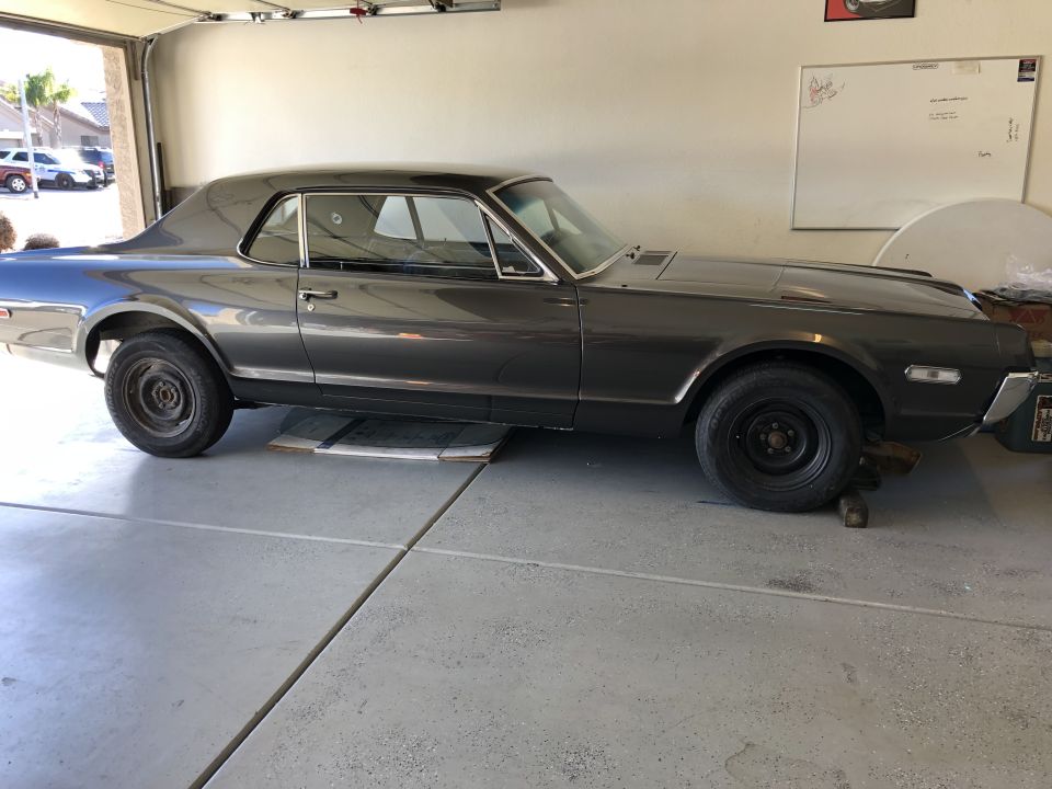 Side view of a dark gray coupe on jack stands in a garage. It has black steel wheels