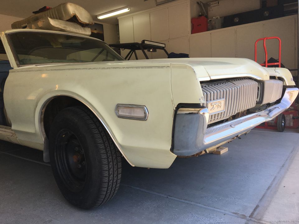 Front end of a cream-colored Mercury Cougar with a vertical grille and a cougar emblem. It's in a garage
