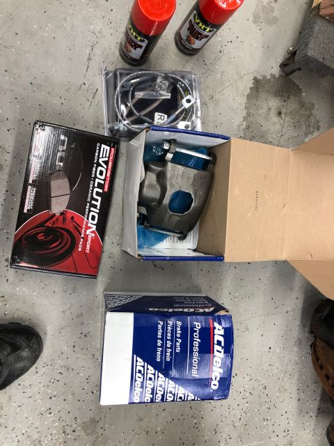 1992 Jeep Wrangler - New brake parts, including a caliper and Evolution brand pads, are laid out on a garage floor.