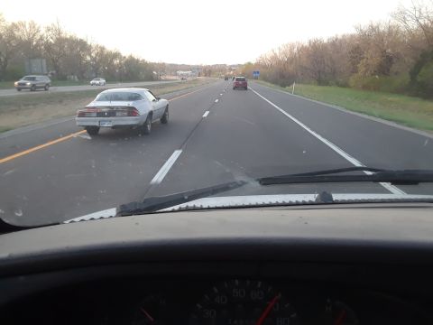 1994 Ford Bronco - A white 1980s Chevrolet Camaro is seen from behind on a highway, with other vehicles in the distance.