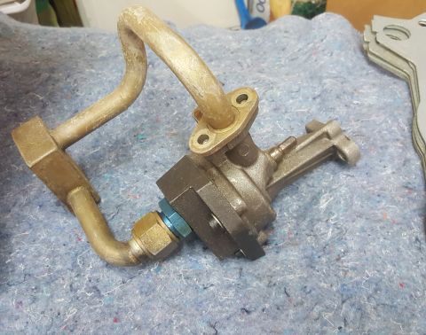 1973 Ford Mustang - A close-up of an oil pump with attached metal tubing and a blue fitting, resting on a textured surface.