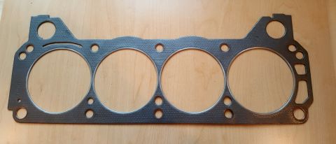 1973 Ford Mustang - A four-cylinder engine gasket is shown flat on a wooden surface, with a website watermark at the bottom right.