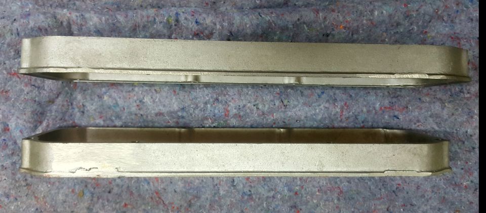 Two silver metal valve covers on a textured gray surface. A logo reads SUPERMOTORS