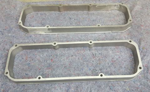1973 Ford Mustang - Two aluminum valve covers are shown side-by-side on a textured gray surface. Text at the bottom right reads "SUPERMOTORS.NET".