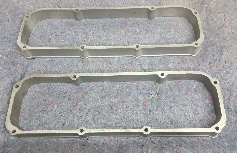 Two silver aluminum valve covers on a gray textured surface